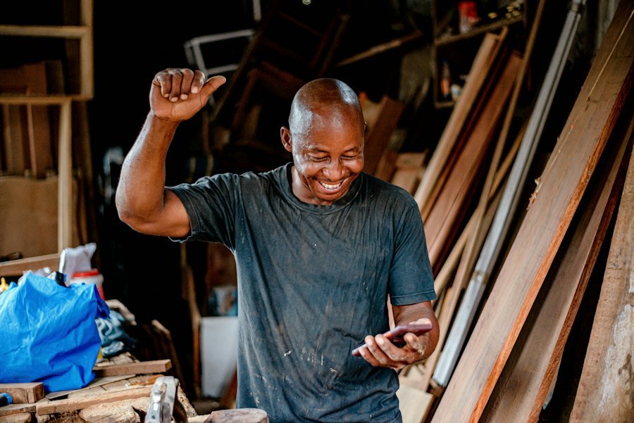 A carpenter in his workshop smiling at his phone